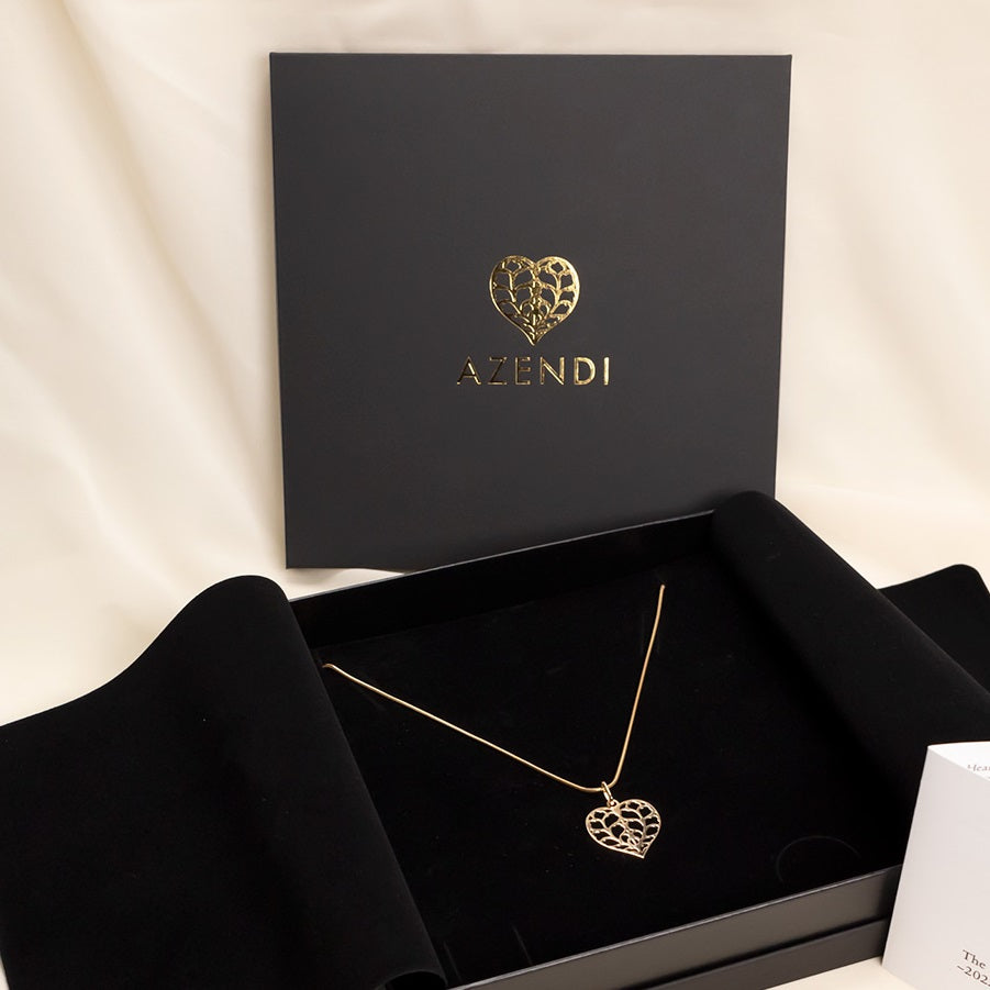 18ct yellow gold heart-shaped pendant with intricate openwork design, displayed on a fine chain within a black presentation box branded with a gold embossed logo.