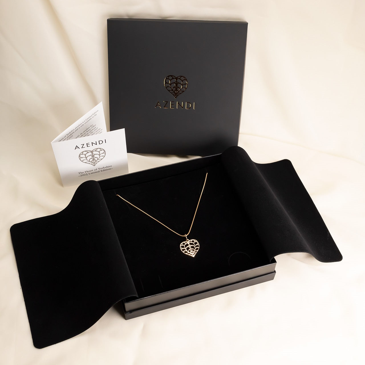 Limited edition 18ct yellow gold pendant featuring an openwork heart design, displayed on a fine chain within an elegant black presentation box by Azendi.