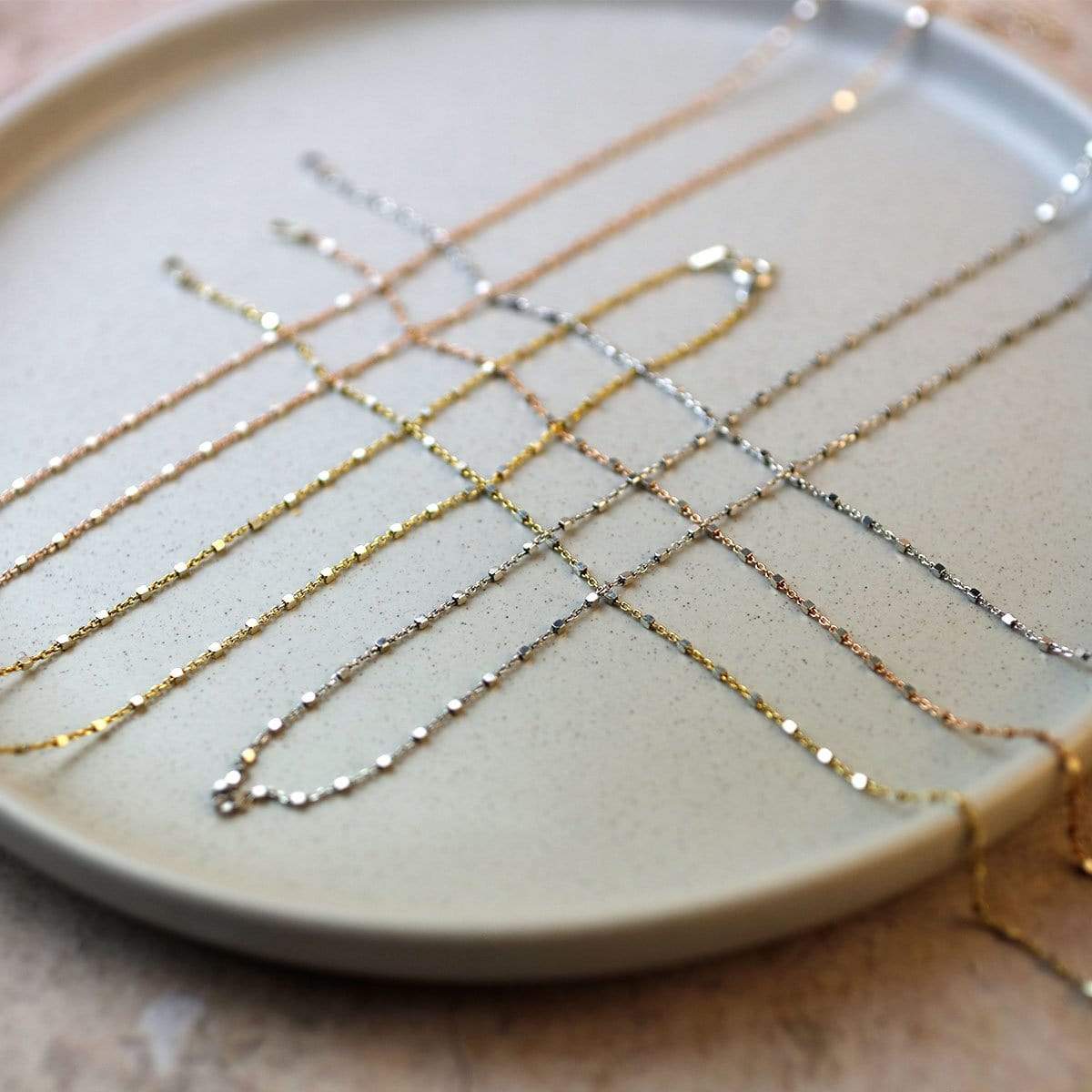 Collection of delicate sterling silver and gold vermeil layering necklaces featuring fine chains with tiny cube-shaped links, showcasing minimalist and sculptural design by Azendi.